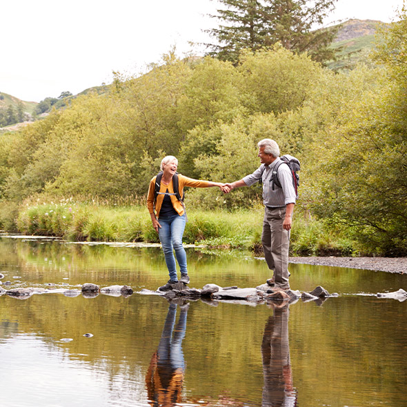 senior couple holding hands while crossing water hiking